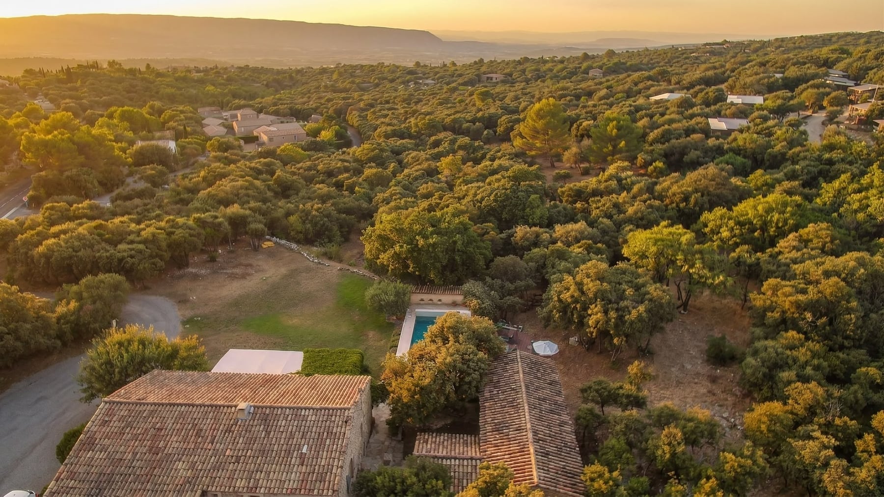 Vue aérienne au couchant : les deux bâtisses, la piscine, le parc et le Luberon
